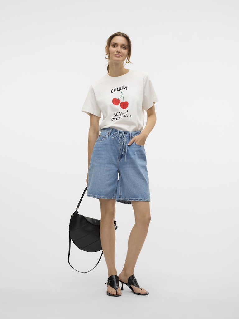 Μοντέλο φοράει VERO MODA λευκό T-shirt με τύπωμα CHERRY, κανονική γραμμή, στρογγυλή λαιμόκοψη, με τζιν βερμούδα