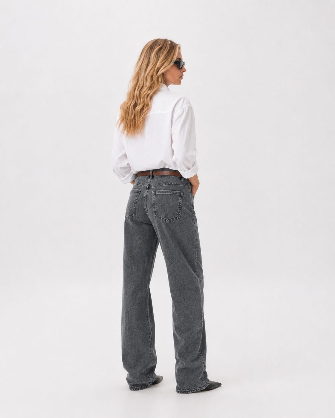 Γυναικείο γκρι πετροπλυμένο baggy τζιν με washed όψη και καφέ ζώνη, πίσω εμφάνιση με λευκό πουκάμισο και μαύρες μυτερές μπότες
