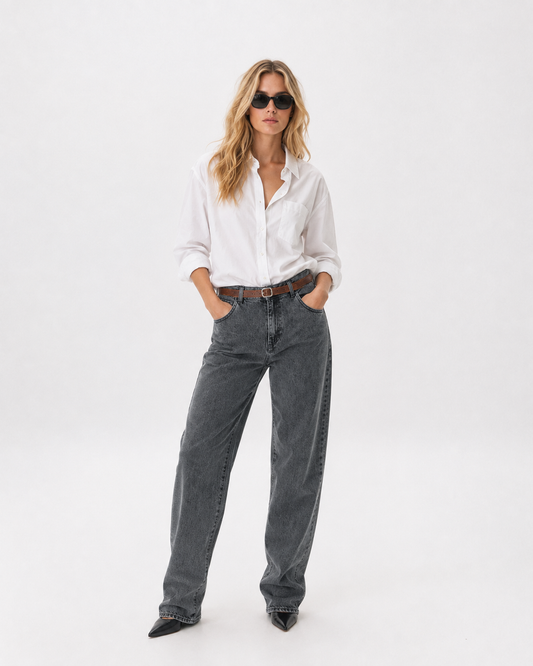 Γυναικείο γκρι πετροπλυμένο baggy τζιν με washed όψη και καφέ ζώνη, ολόσωμη εμφάνιση με λευκό πουκάμισο και μαύρες μυτερές μπότες
