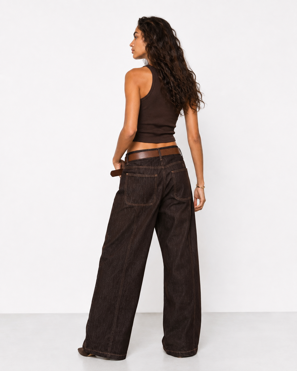 Γυναικείο καφέ baggy jeans με ψηλή μέση, μεγάλες πίσω τσέπες και καφέ δερμάτινη ζώνη, πίσω εμφάνιση με καφέ crop top και καφέ μποτάκια
