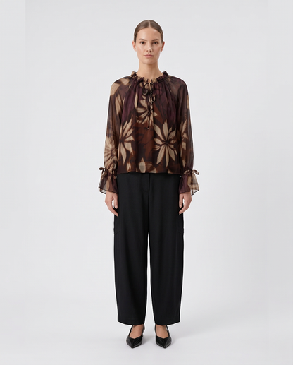 Γυναικεία μωβ floral μπλούζα georgette με σούρες και δεσίματα, ολόσωμη εμφάνιση με μαύρο παντελόνι
