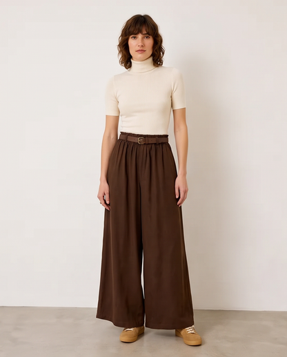 Γυναικεία σκούρο καφέ παντελόνα βισκόζη με ελαστική μέση, ζώνη δώρο και αέρινη ευρεία γραμμή, ολόσωμη εμφάνιση με εκρού ζιβάγκο και sneakers

