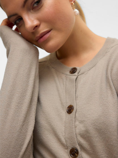 Κοντινή λήψη της στρογγυλής λαιμόκοψης και των διακοσμητικών κουμπιών της μπεζ ζακέτας VERO MODA